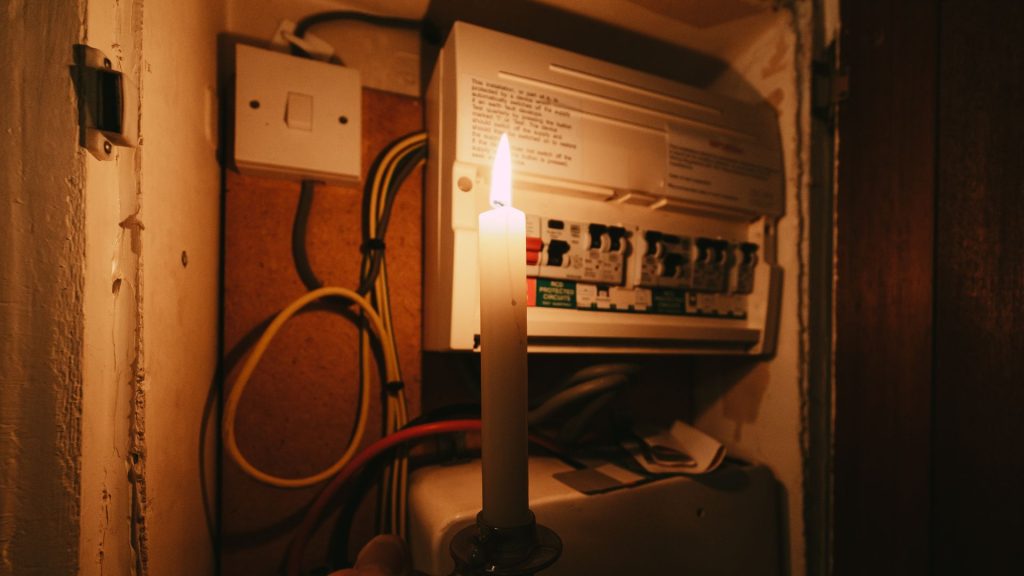 A person holding a lit candle next to an electric panel
