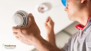 A person wearing a hard hat is holding a smoke detector